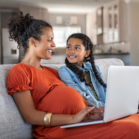 pregnant woman working on her laptop while young girl smiles at her